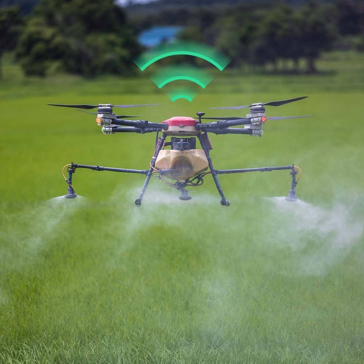 A drone equipped with smart sensors spraying liquid fertilizer over a green agricultural field, using IIoT connectivity to ensure precise application and real-time monitoring for smarter farming.
