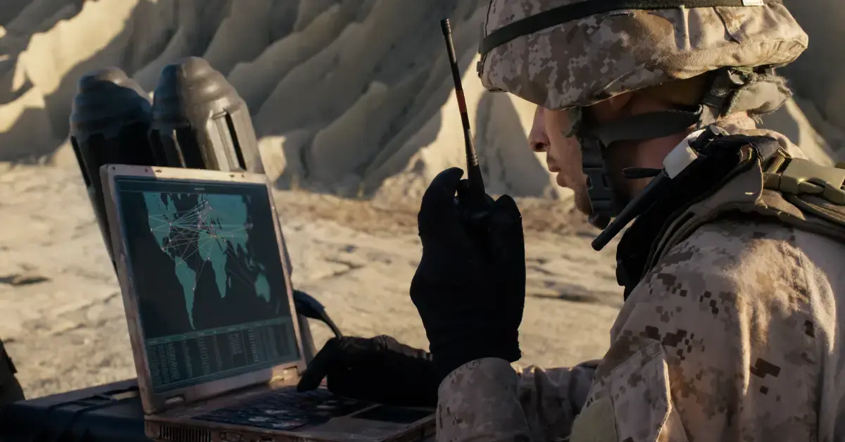 Soldier in tactical gear monitoring biometric and environmental sensors via IoT connectivity on a rugged handheld device, defence battlefield setting.