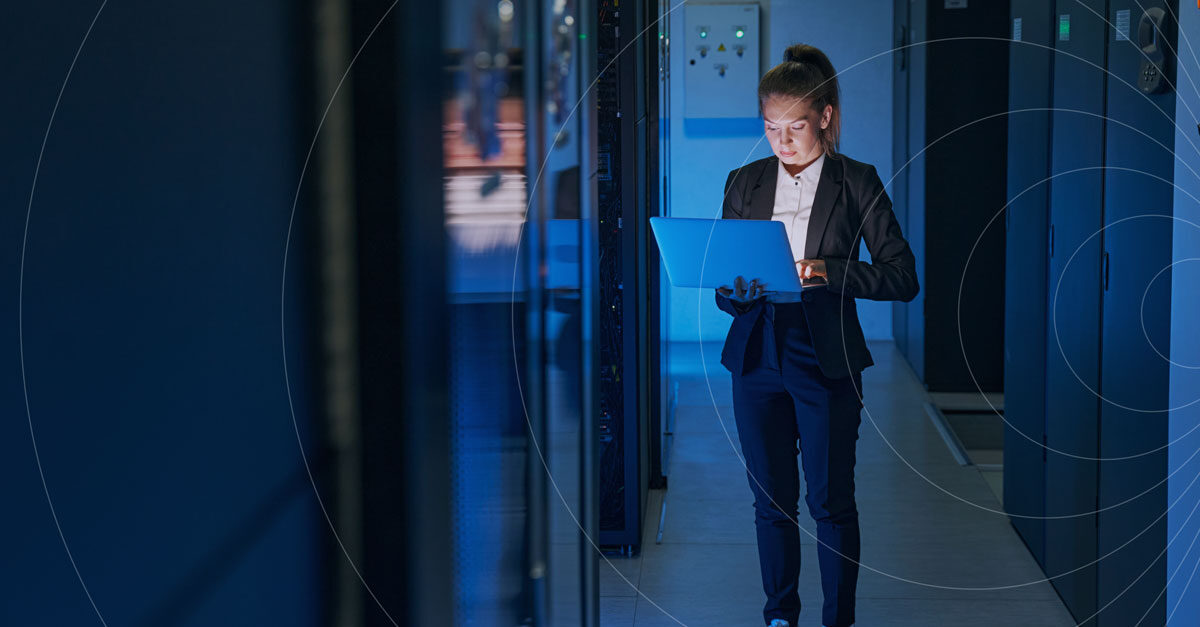 IT professional in business attire walking through a blue-lit data center server aisle while checking a laptop, with a concentric-circle connectivity graphic overlaid on the image.