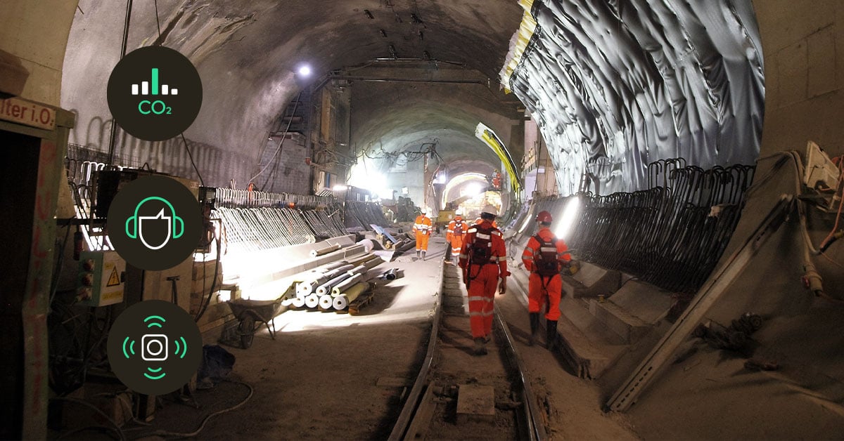 Construction worker inside a tunnel using IoT sensors to measure temperature, humidity, and moisture levels for safety and quality control.