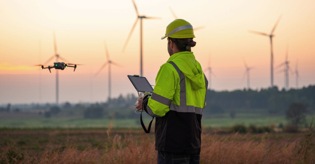IoT-connected drone assisting engineer in inspecting wind turbines for maintenance.
