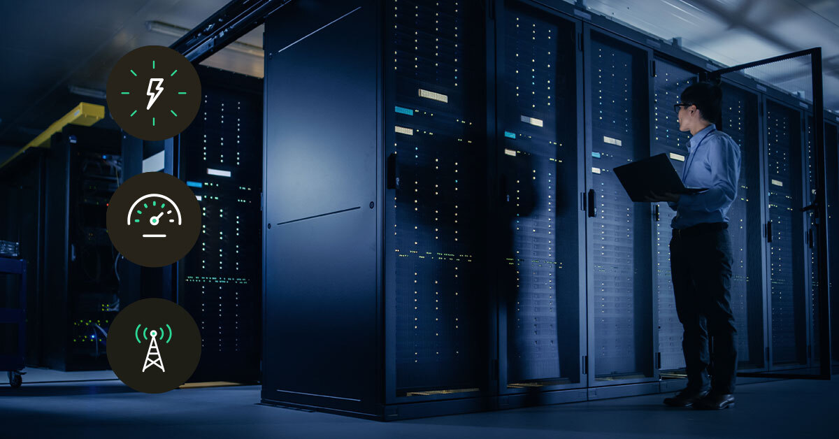 Technician stands in a cold-aisle between server racks, checking performance and uptime on a laptop for network operations and security compliance.
