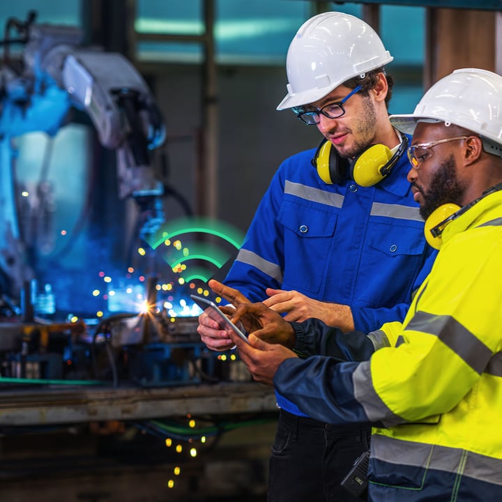 To ingeniører med vernehjelm inspiserer IoT-tilkoblede sensorer i en fabrikk