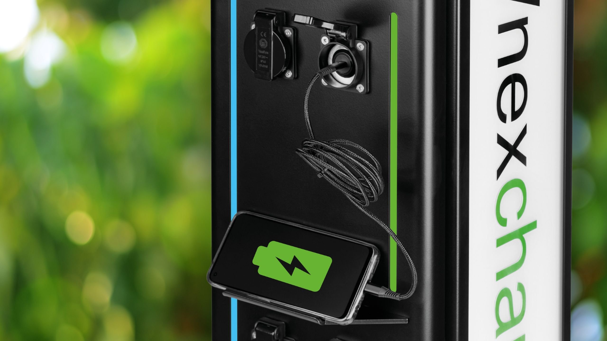 Close-up of a black NexCharge charging station with a smartphone charging by cable on its built-in shelf
