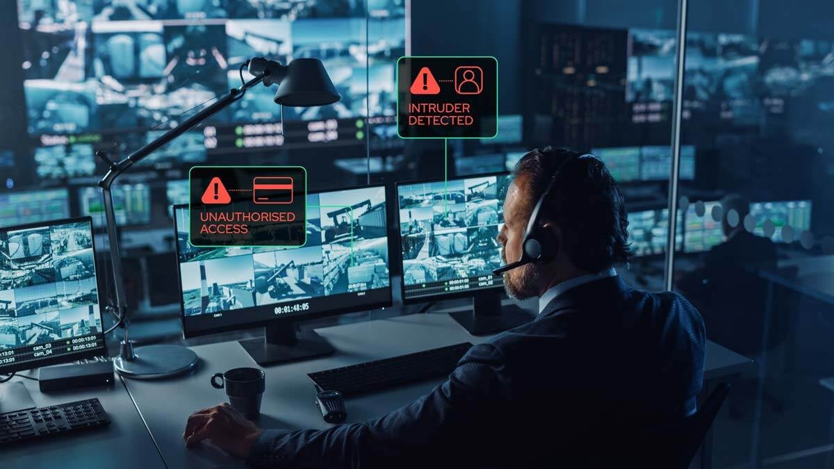Security guard monitoring a construction site through CCTV cameras on multiple screens in a control room