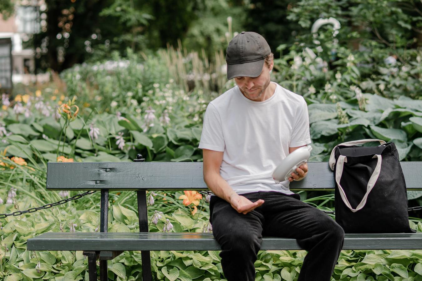 Man sitting in a park using a connected pill dispenser device for medication management, illustrating IoT healthcare connectivity
