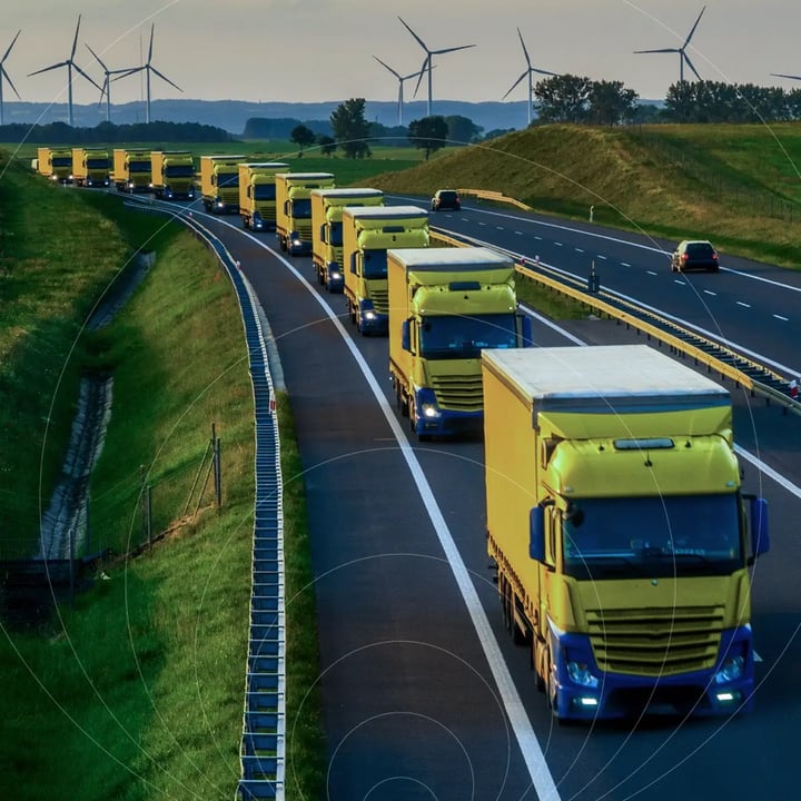 A convoy of yellow trucks travels along a highway lined with wind turbines, overlaid with concentric ring graphics symbolizing IoT connectivity tracking each vehicle.