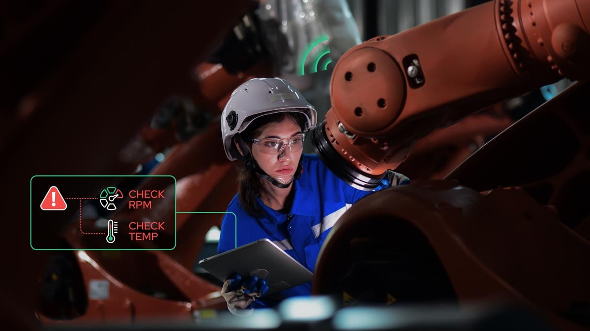 Female technician wearing a safety helmet, performing maintenance on an IoT device in an industrial facility, surrounded by machinery and control panels