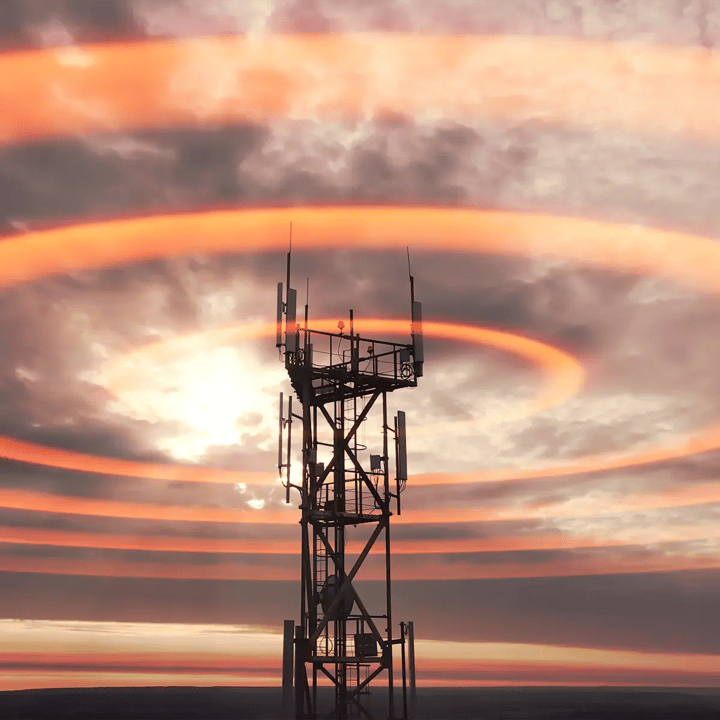 A cellular network tower silhouetted against a dramatic orange sunset sky, with concentric ripple-like rings radiating outward from the antennas across the clouds to suggest wireless signal propagation.