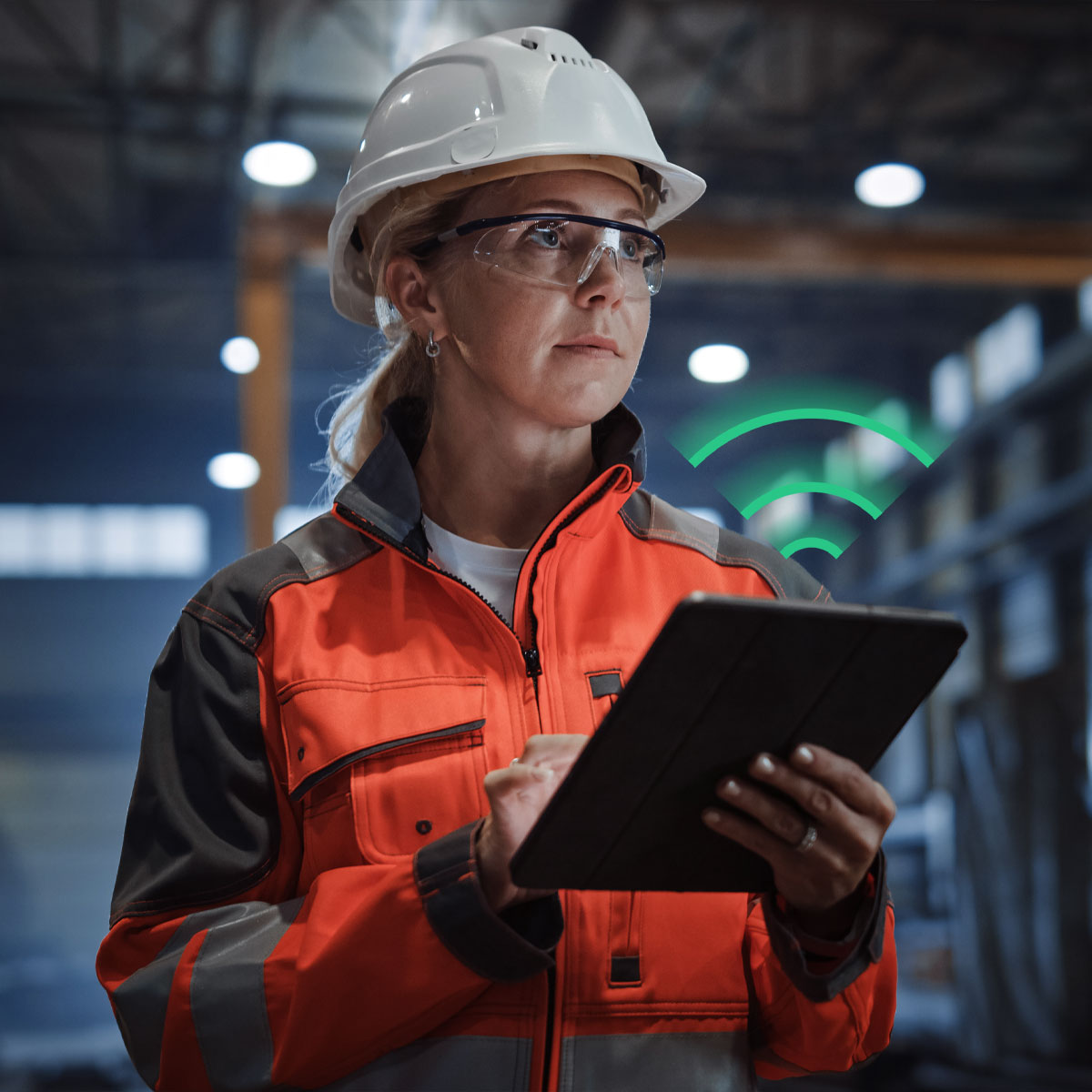 An industrial worker in hi-vis safety gear uses a tablet on a factory floor, with a green wifi-signal graphic representing LPWA cellular IoT connectivity (NB-IoT/LTE-M) monitoring industrial equipment in real time.