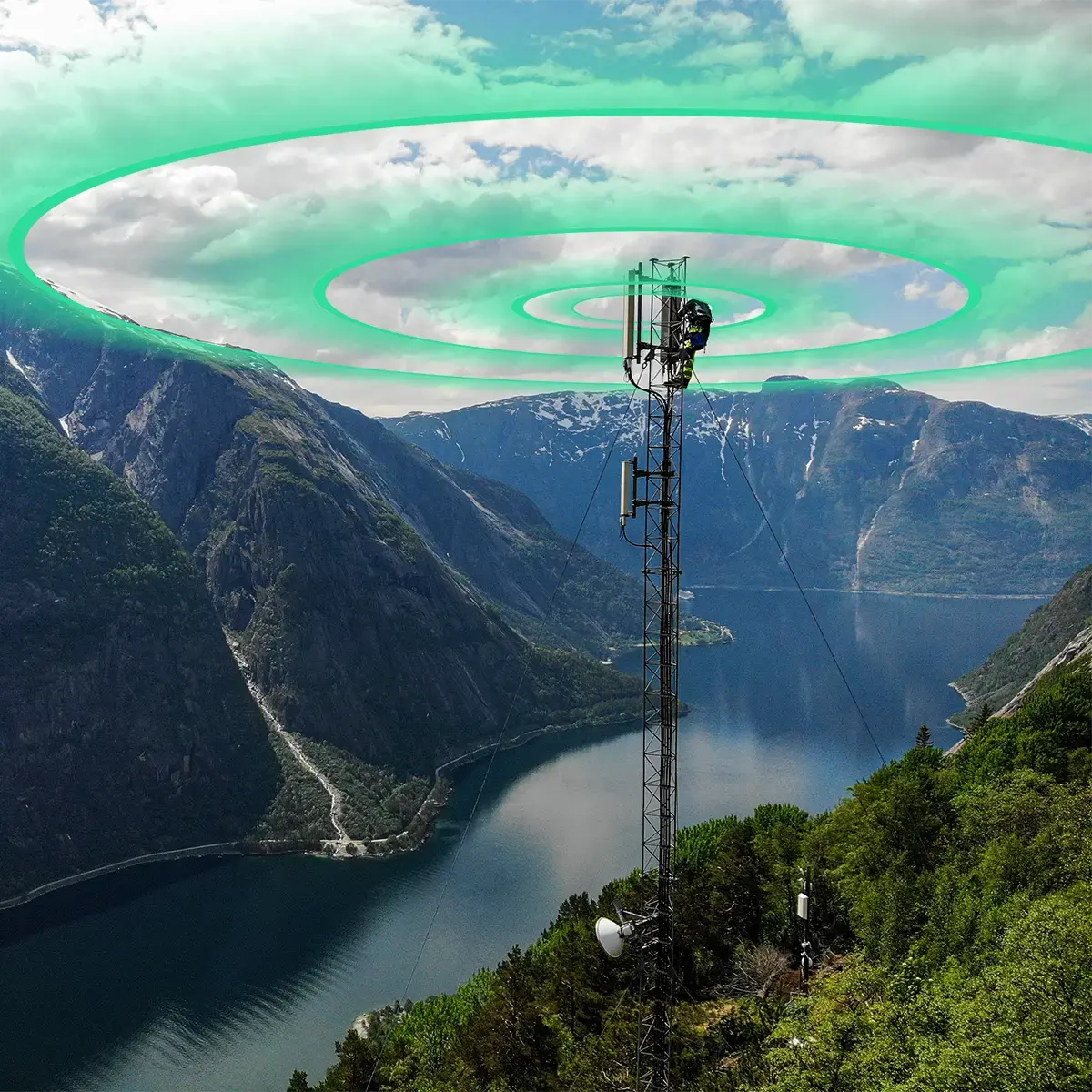 Cellular network tower on a mountain ridge overlooking a Norwegian fjord, with a technician working at the top and green signal rings radiating outward to represent network coverage.